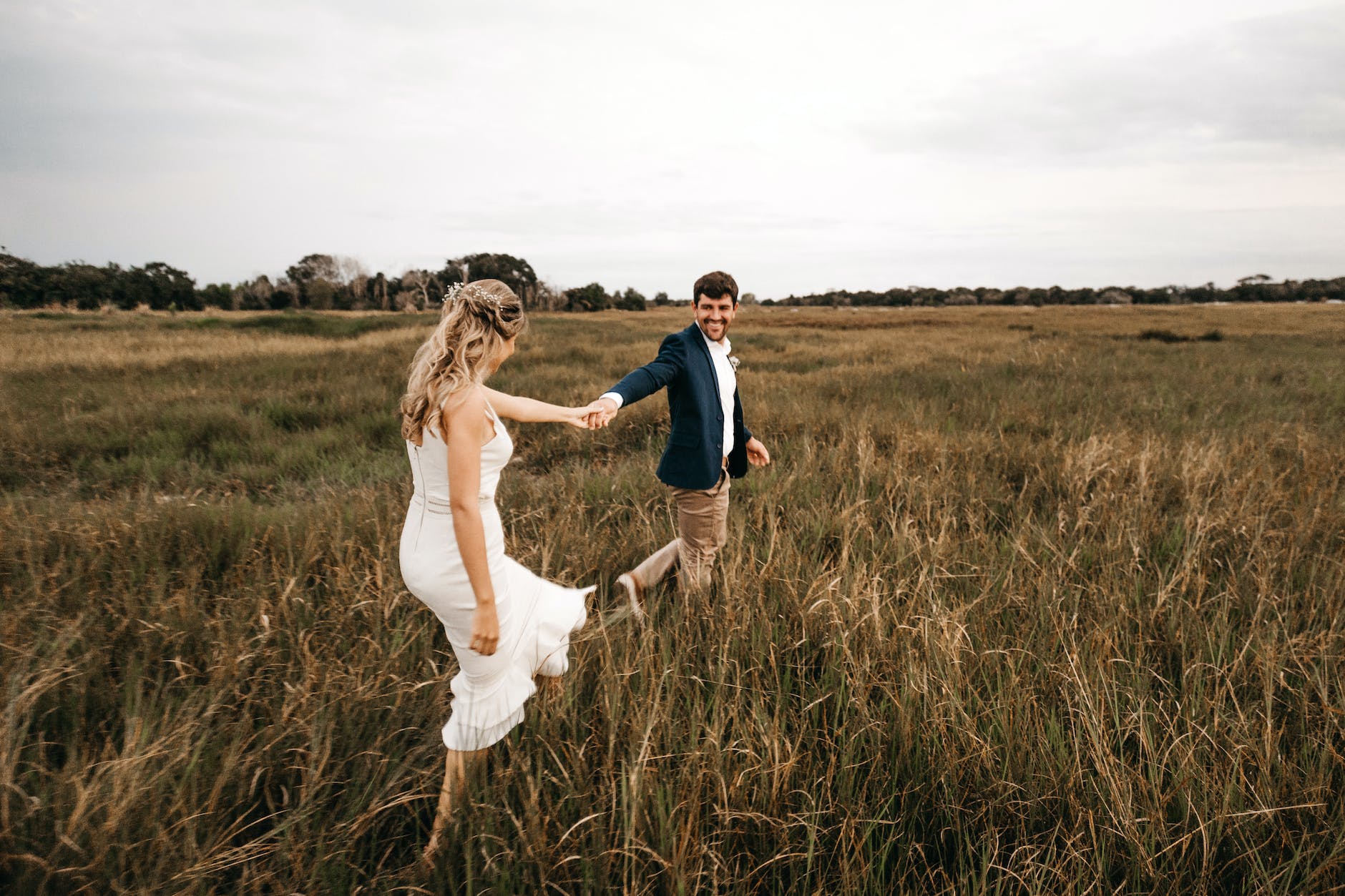 outdoor couple photoshoot - A bride and groom walking through a field of tall grass.