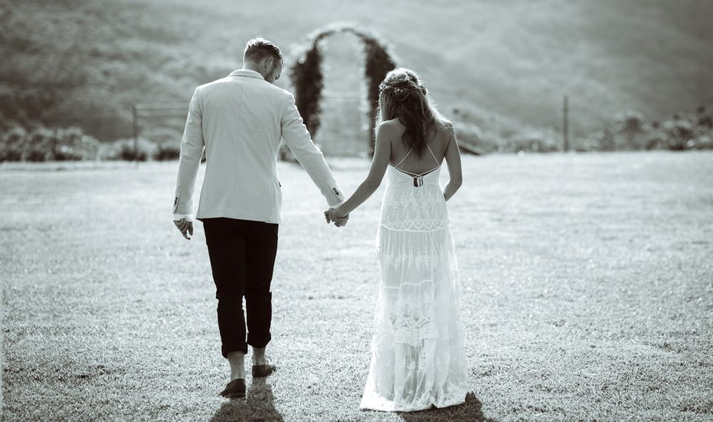 A bride and groom showcasing pre-wedding poses as they joyfully hold hands in a picturesque field.