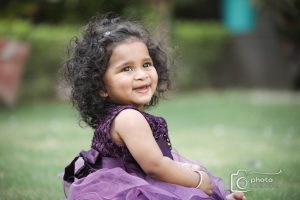 A little girl in a purple dress engrossed in stories while sitting on the grass.